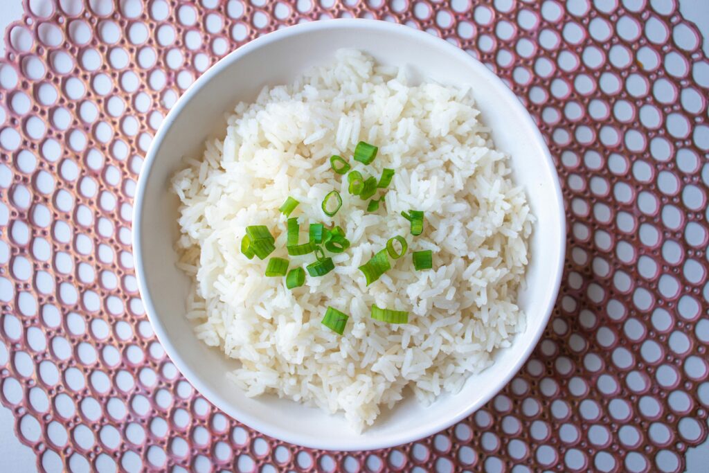 A bowl of cooked white rice garnished with green onions, perfect for culinary presentations.